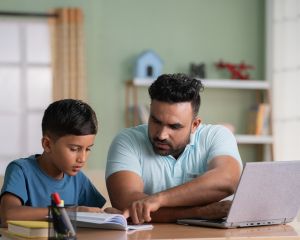 Man working on computer while pointing at child's notebook
