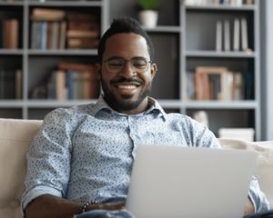 Man sitting on couch, smiling and working on a computer