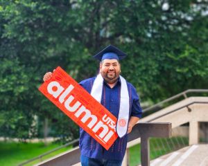 Roger Ruiz holding a "UTSA Alumni" banner