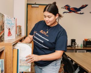 Teacher wearing UTSA t-shirt putting a book in a bookshelf