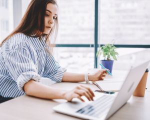Woman working on computer and writing in a notebook