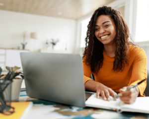 Woman smiling and writing while looking at a computer